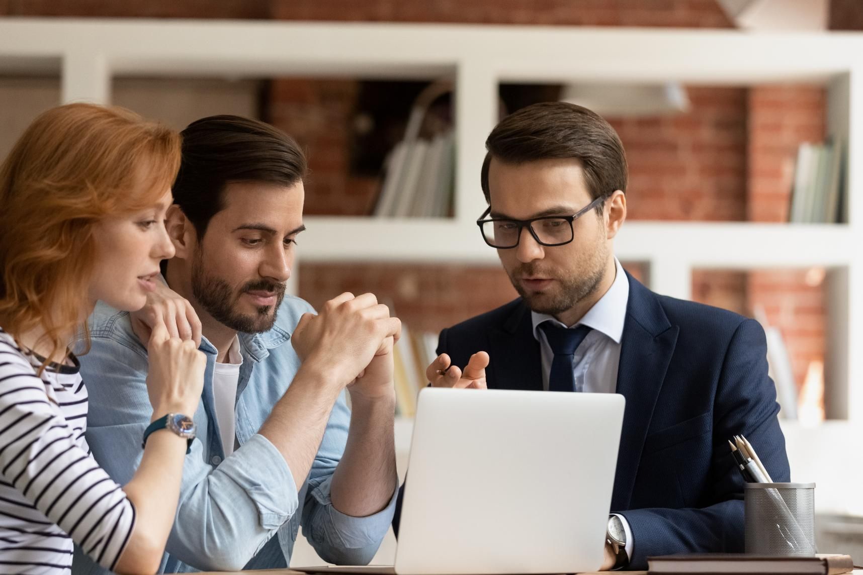 A financial advisor in a suit showing a laptop to a concerned couple, indoor setting.